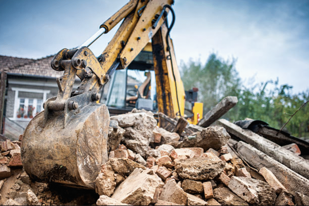 A bulldozer is excavating rubble in front of a house, clearing debris from the construction site.